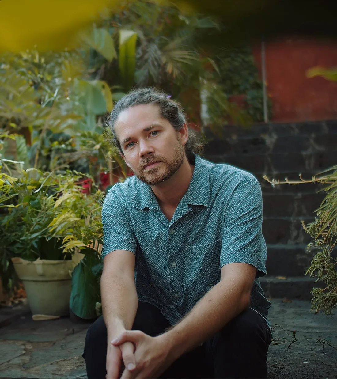 Holden Davies seated on stone steps in a garden, looking into the camera